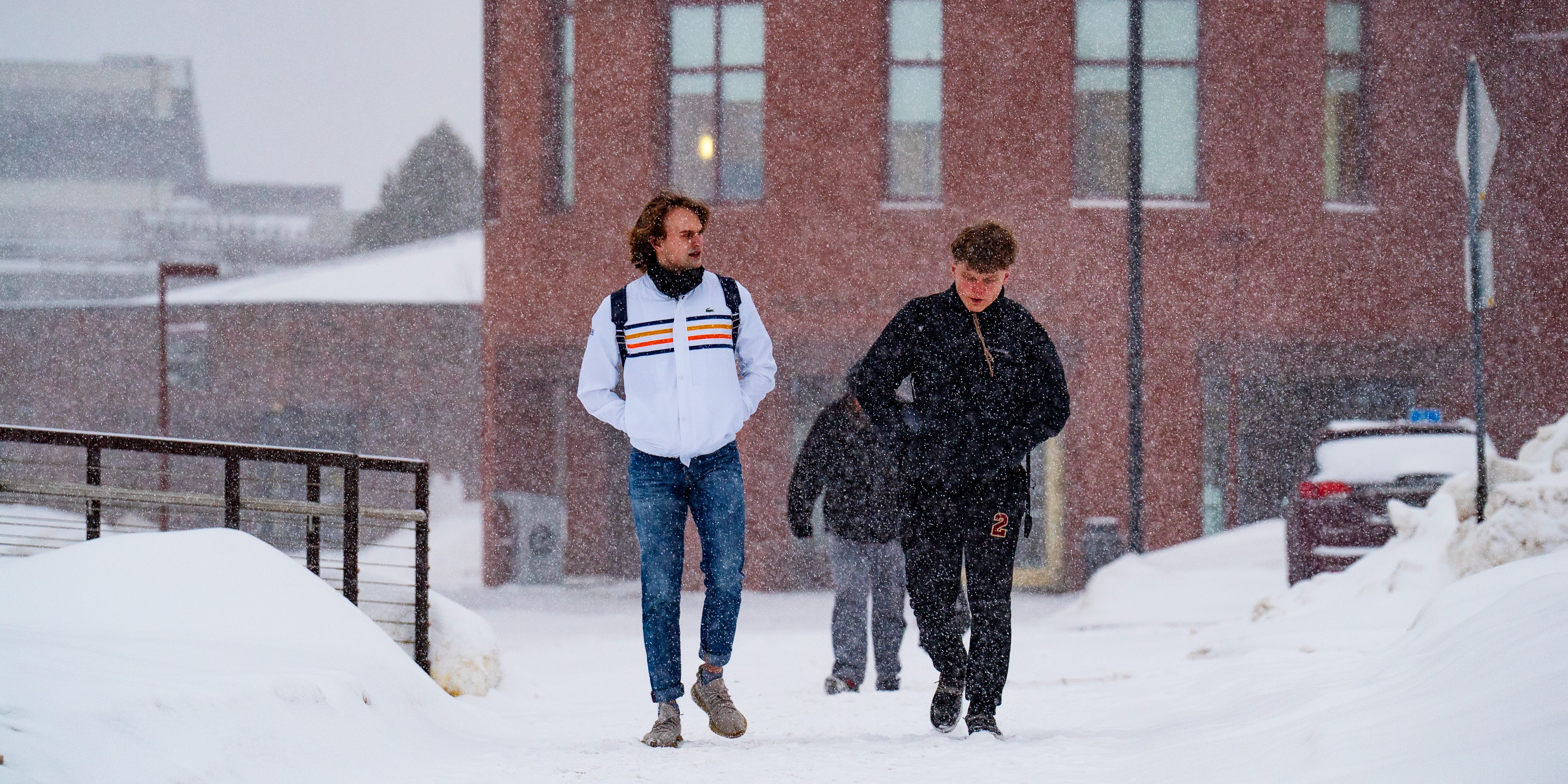 Two students walk across a very snowy campus wearing coats